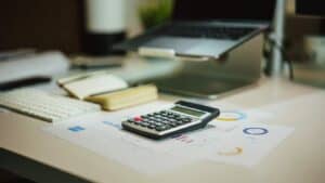 Calculator on a desk next to printed charts, a keyboard and a laptop