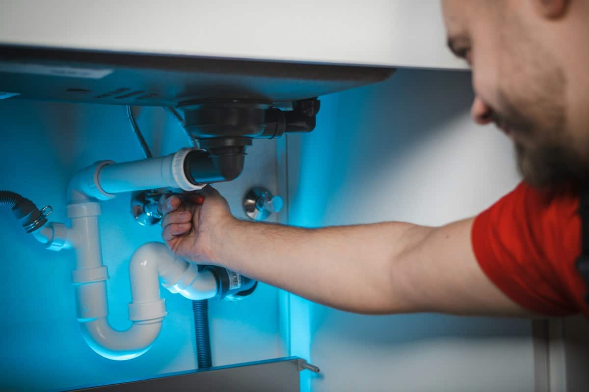 Plumber fixing the drain pipes under a sink