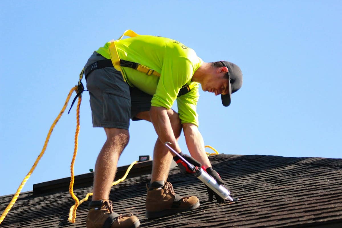 Roofer in a safety harness installing shingles